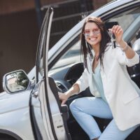 Young attractive woman just bought a new car. female holding keys from new automobile.